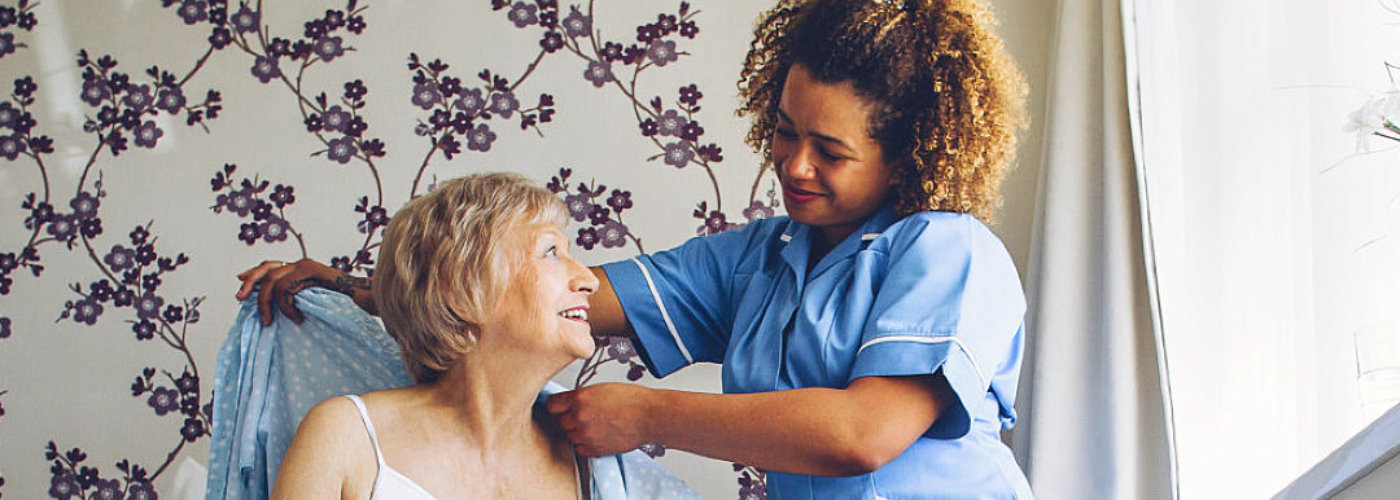 caregiver assisting senior woman to dress up